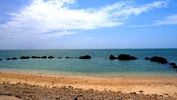 View of Shiraho Beach with turquoise waters and dark coral rocks scattered along the shoreline under a clear blue sky in Ishigaki Okinawa Japan.