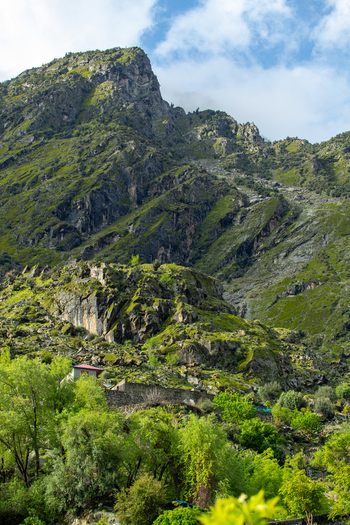 View of a steep rocky mountain covered in green vegetation with lush trees and a small building in the foreground Chilas Gilgit Pakistan. View of a steep rocky mountain covered in green vegetation with lush trees and a small building in the foreground Chilas Gilgit Pakistan.