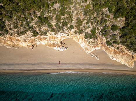 Aerial view of Cala Luna beach with turquoise water golden sand limestone cliffs and a person walking on the shore in Baunei Sardegna Italy. Aerial view of Cala Luna beach with turquoise water golden sand limestone cliffs and a person walking on the shore in Baunei Sardegna Italy.