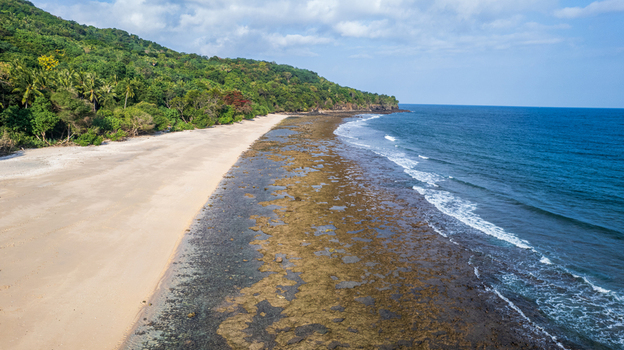 Aerial view of a sandy beach with a rocky shoreline and lush green hills meeting the blue sea in Bajawa Nusa Tenggara Timur Indonesia. Aerial view of a sandy beach with a rocky shoreline and lush green hills meeting the blue sea in Bajawa Nusa Tenggara Timur Indonesia.