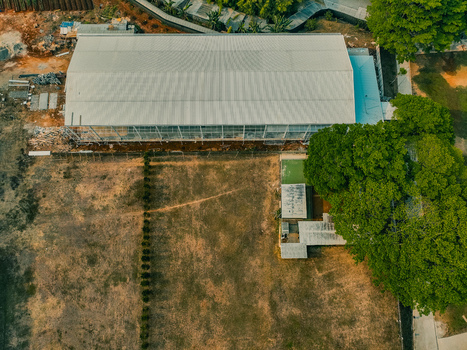 Aerial view of The Pavilion Venue featuring a large rectangular building with a metal roof surrounded by a grassy field and lush trees in Kecamatan Ciputat Timur Banten Indonesia. Aerial view of The Pavilion Venue featuring a large rectangular building with a metal roof surrounded by a grassy field and lush trees in Kecamatan Ciputat Timur Banten Indonesia.
