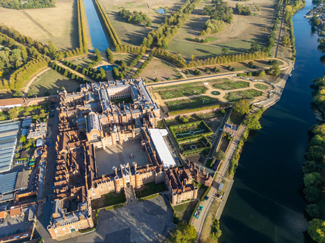 Aerial view of Hampton Court Palace with its historic red brick architecture formal gardens and surrounding parkland situated along the River Thames in Molesey England United Kingdom. Aerial view of Hampton Court Palace with its historic red brick architecture formal gardens and surrounding parkland situated along the River Thames in Molesey England United Kingdom.