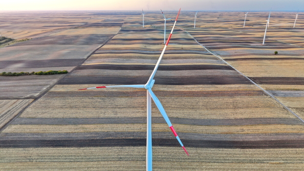 Aerial view of wind turbines standing in vast agricultural fields with striped patterns during golden hour in Vladimirovac Vojvodina Serbia.
