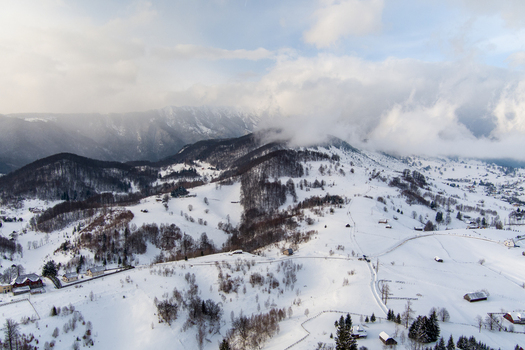 Brasov Romania 21 September 2026 Aerial view of the snow covered Carpathian Mountains near Brasov featuring rolling hills scattered wooden cabins and dense forests under a cloudy sky. Brasov Romania 21 September 2026 Aerial view of the snow covered Carpathian Mountains near Brasov featuring rolling hills scattered wooden cabins and dense forests under a cloudy sky.