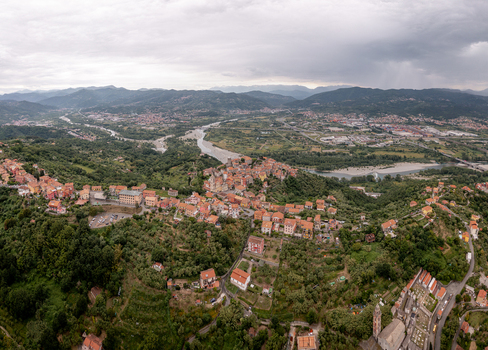 Aerial view of the historic village of Vezzano Ligure featuring terracotta rooftops surrounding green hills and the Magra river valley under a cloudy sky in Vezzano Ligure Liguria Italy.