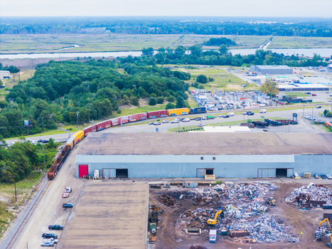 Wilmington United States 18 September 2026 Aerial view of a freight train passing by an industrial warehouse and a scrap metal yard with piles of debris and heavy machinery.