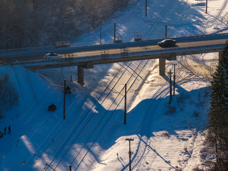 Aerial view of a road bridge crossing over snow covered railway tracks with people and quad bikes in a wintry forest with long shadows in Lithuania. Aerial view of a road bridge crossing over snow covered railway tracks with people and quad bikes in a wintry forest with long shadows in Lithuania.