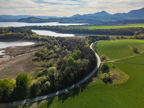 Aerial view of a winding road through green fields and forest near the Liptovska Mara reservoir with mountains in the distance Liptovsky Trnovec Zilina Region Slovakia.