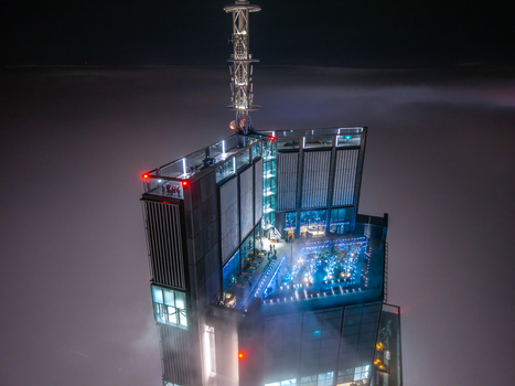Aerial view of a modern skyscraper rooftop with an illuminated observation deck and antenna tower surrounded by thick fog at night in Poland. Aerial view of a modern skyscraper rooftop with an illuminated observation deck and antenna tower surrounded by thick fog at night in Poland.