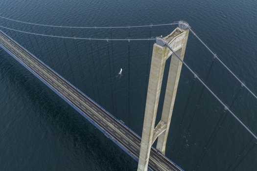 Aerial view of the Great Belt Bridge pylon and suspension cables over the dark blue sea with a small sailboat below Denmark. Aerial view of the Great Belt Bridge pylon and suspension cables over the dark blue sea with a small sailboat below Denmark.