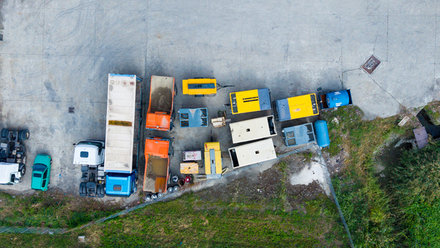 Aerial view of construction machinery including dump trucks trailer mounted diesel generators and a car parked on a concrete lot in Milan Lombardy Italy.