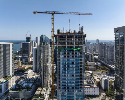 Aerial view of a skyscraper under construction with a crane towering over the city skyline against a clear blue sky Miami Florida USA. Aerial view of a skyscraper under construction with a crane towering over the city skyline against a clear blue sky Miami Florida USA.