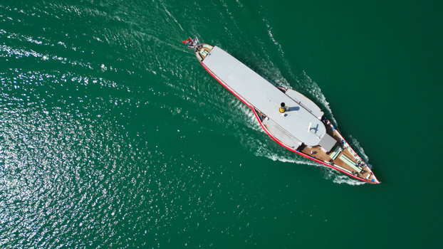 Aerial view of a vintage boat sailing across the serene waters of Lake Neuchâtel the vessel s red trim sharply contrasting with the deep green of the lake Neuchâtel Neuchâtel Switzerland. Aerial view of a vintage boat sailing across the serene waters of Lake Neuchâtel the vessel s red trim sharply contrasting with the deep green of the lake Neuchâtel Neuchâtel Switzerland.