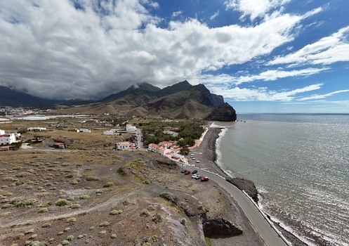 Aerial view of dark volcanic sands meeting the turquoise ocean a rugged coastline contrasting with the distant mountains Puerto de la Aldea Canarias Spain. Aerial view of dark volcanic sands meeting the turquoise ocean a rugged coastline contrasting with the distant mountains Puerto de la Aldea Canarias Spain.