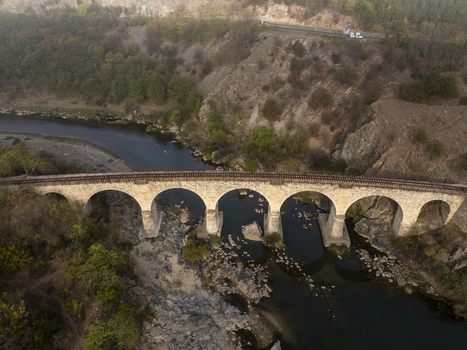 Aerial view of the historic stone railway bridge spanning a river in a hilly landscape with rocky banks and lush vegetation in Balabanovo Kardzhali Province Bulgaria. Aerial view of the historic stone railway bridge spanning a river in a hilly landscape with rocky banks and lush vegetation in Balabanovo Kardzhali Province Bulgaria.