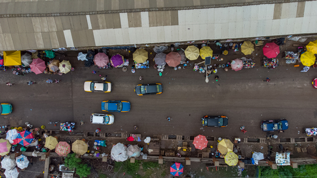 Aerial view of the bustling Elmina market with colorful umbrellas street vendors and cars moving along the road in Elmina Central Region Ghana. Aerial view of the bustling Elmina market with colorful umbrellas street vendors and cars moving along the road in Elmina Central Region Ghana.