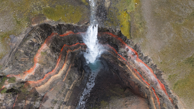 Aerial view of Hengifoss waterfall cutting through layered basalt cliffs with striking red clay bands Hengifoss Iceland.