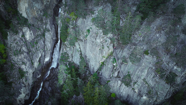 Aerial view of Gorges du Dailley waterfall cascading down a steep rocky cliff with wooden stairs and pine trees in Salvan Valais Switzerland.