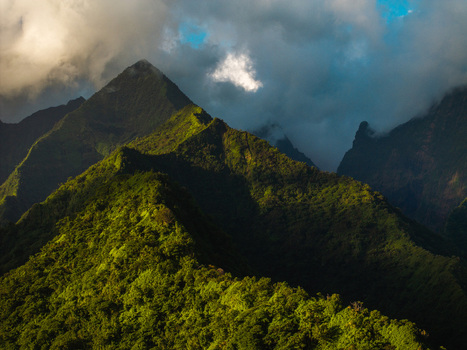 Aerial view of lush volcanic mountain ridges and sharp peaks shrouded in dramatic clouds under soft sunlight Moorea Maiao Windward Islands French Polynesia. Aerial view of lush volcanic mountain ridges and sharp peaks shrouded in dramatic clouds under soft sunlight Moorea Maiao Windward Islands French Polynesia.