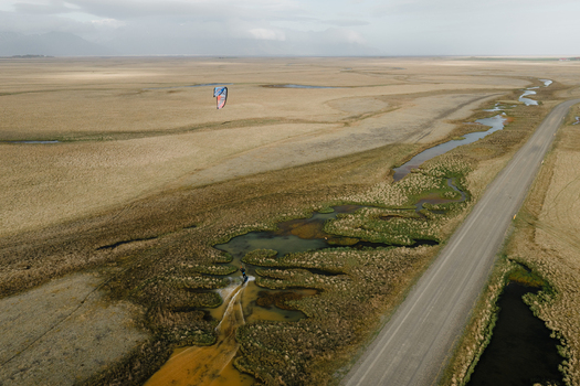 Aerial view of a kite surfer gliding through a winding stream in the wetlands near a gravel road in Hofn Sveitarfelagid Hornafjordur Iceland.