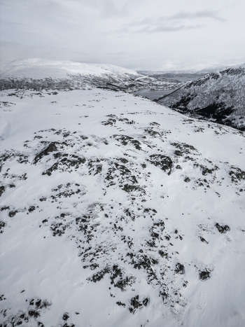 Aerial view of a snow covered mountain ridge with rocky outcrops overlooking a fjord under an overcast sky Ersfjord Troms Norway. Aerial view of a snow covered mountain ridge with rocky outcrops overlooking a fjord under an overcast sky Ersfjord Troms Norway.