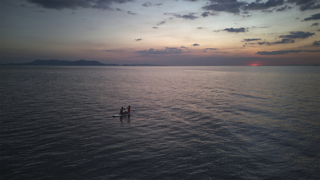 Aerial view of two people on a paddleboard on the calm sea at Jomtien Beach during a vibrant sunset with distant hills Chon Buri Thailand.