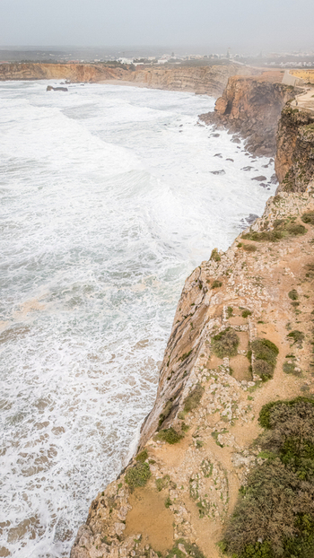 Aerial view of the dramatic cliffs of Sagres overlooking the churning Atlantic Ocean with white foam and misty horizon Sagres Faro Portugal. Aerial view of the dramatic cliffs of Sagres overlooking the churning Atlantic Ocean with white foam and misty horizon Sagres Faro Portugal.