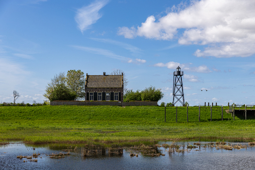 View of the historic lighthouse keeper s house and iron lighthouse tower on the former island of Schokland with green meadows and marshy water under a blue sky Schokland Flevoland Netherlands.