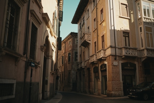 View of historic buildings along a narrow street with ornate balconies and warm sunlight in the old town of Verona Veneto Italy.