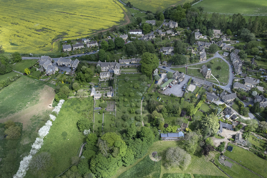 Aerial view of Snowshill Manor surrounded by historic stone cottages lush gardens and rolling green fields in the Cotswolds Snowshill England United Kingdom.