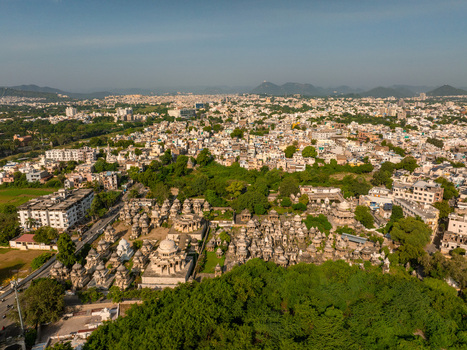 Aerial view of the historic Ahar Cenotaphs featuring numerous stone domes and monuments surrounded by lush trees and the urban landscape of Udaipur Rajasthan India.