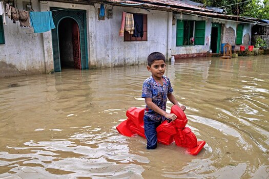 Banshkhali Upazila Chittagong Division Bangladesh 10 July 2026 View of a young boy playing on a red plastic toy motorcycle in floodwaters in front of a house. Banshkhali Upazila Chittagong Division Bangladesh 10 July 2026 View of a young boy playing on a red plastic toy motorcycle in floodwaters in front of a house.