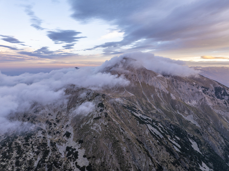 Aerial view of Pirin National Park with rugged mountain peaks partially covered by clouds under a soft twilight sky in Blagoevgrad Province Bulgaria. Aerial view of Pirin National Park with rugged mountain peaks partially covered by clouds under a soft twilight sky in Blagoevgrad Province Bulgaria.