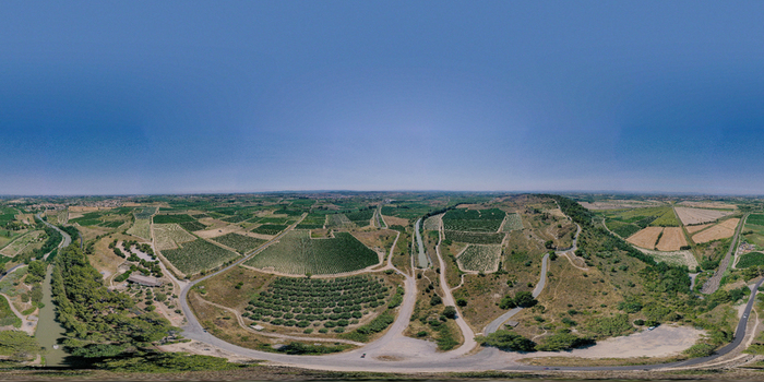 Aerial view of the Tunnel le Malpas area with lush vineyards agricultural fields and winding roads under a clear blue sky in Nissan lez Enserune Occitanie France.