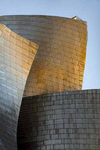 View of the curved titanium panels of the Guggenheim Museum Bilbao reflecting golden sunlight against a clear blue sky in Bilbao Euskadi Spain. View of the curved titanium panels of the Guggenheim Museum Bilbao reflecting golden sunlight against a clear blue sky in Bilbao Euskadi Spain.