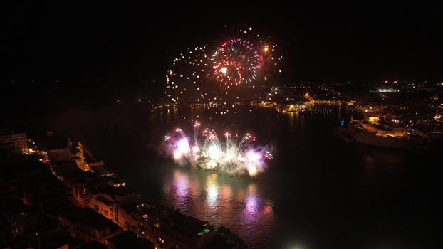 Aerial view of a vibrant fireworks display illuminating the Grand Harbour at night with reflections on the water and the historic city skyline in Valletta Port Region Malta. Aerial view of a vibrant fireworks display illuminating the Grand Harbour at night with reflections on the water and the historic city skyline in Valletta Port Region Malta.