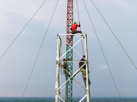 Trishal Upazila Bangladesh 13 May 2026 Aerial view of workers climbing a tall telecommunications tower with a red and green lattice structure against a cloudy sky. Trishal Upazila Bangladesh 13 May 2026 Aerial view of workers climbing a tall telecommunications tower with a red and green lattice structure against a cloudy sky.
