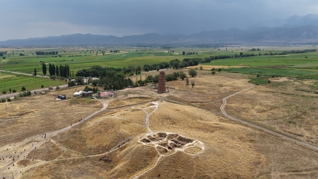 Aerial view of the historic Burana Tower minaret surrounded by ancient archaeological mounds green fields and distant mountains in Tokmak Chuy Province Kyrgyzstan. Aerial view of the historic Burana Tower minaret surrounded by ancient archaeological mounds green fields and distant mountains in Tokmak Chuy Province Kyrgyzstan.