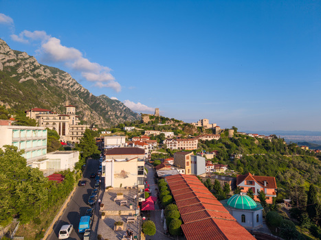 Kruje Albania 12 June 2026 Aerial view of the historic town featuring Kruje Castle on a hill red tiled rooftops and a green domed mosque against the Skanderbeg Mountains.