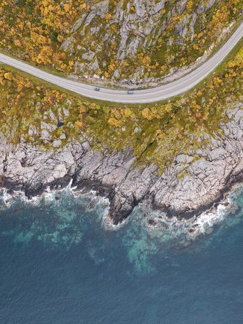 Aerial view of the coastal road winding along the rocky cliffs of Lofoten featuring vibrant autumn foliage and the deep blue sea in Svolvaer Nordland Norway.