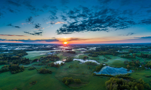 Aerial view of a rural landscape featuring green fields small ponds and morning mist under a dramatic sunrise sky in Latvia. Aerial view of a rural landscape featuring green fields small ponds and morning mist under a dramatic sunrise sky in Latvia.