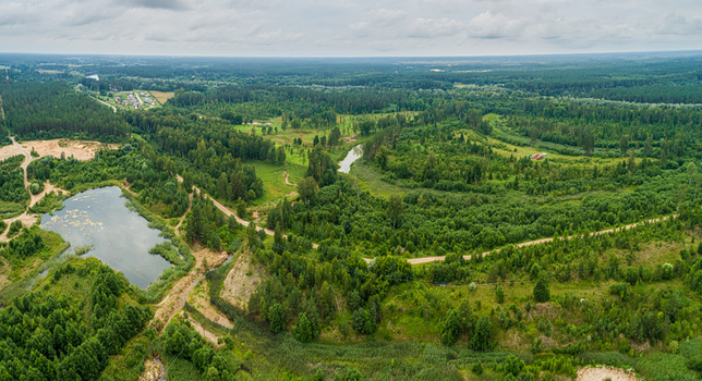 Aerial view of a serene landscape featuring a small lake a winding dirt road and dense green forests under an overcast sky in Latvia. Aerial view of a serene landscape featuring a small lake a winding dirt road and dense green forests under an overcast sky in Latvia.