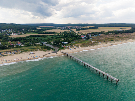 Aerial view of a long pier extending into the turquoise waters of the Black Sea at the sandy beach with green coastal hills and a cloudy sky Shkorpilovtsi Varna Bulgaria. Aerial view of a long pier extending into the turquoise waters of the Black Sea at the sandy beach with green coastal hills and a cloudy sky Shkorpilovtsi Varna Bulgaria.