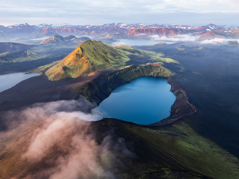 Aerial view of a volcanic crater lake nestled among dark lava fields and moss covered peaks reflects the ethereal light of Iceland s highlands Highlands Iceland.