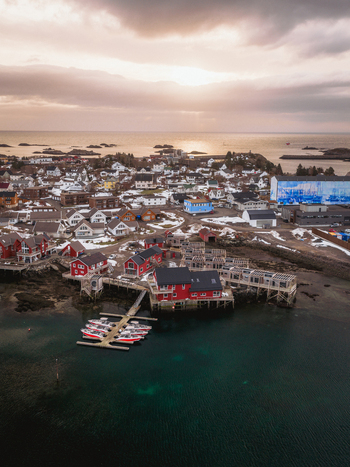 Aerial view of the vibrant red buildings contrast against the dark waters and the snowy landscape of Ballstad Nordland Norway. Aerial view of the vibrant red buildings contrast against the dark waters and the snowy landscape of Ballstad Nordland Norway.