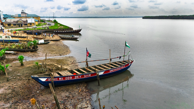 Aerial view of colorful wooden boats moored along the muddy riverbank with calm water and a cloudy sky in the background Minima Rivers Nigeria.