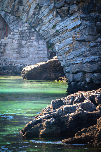 View of the historic stone archway and rugged coastal rocks overlooking the turquoise waters of the Atlantic Ocean in Cascais Lisbon Portugal.