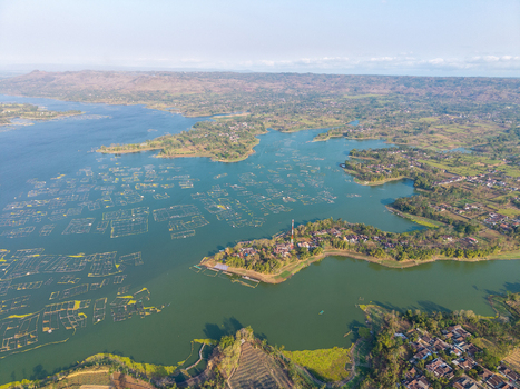Aerial view of Sutami Dam in Karangkates featuring fish farming cages on the reservoir surrounded by lush hills and rural settlements in Kecamatan Sumberpucung Jawa Timur Indonesia. Aerial view of Sutami Dam in Karangkates featuring fish farming cages on the reservoir surrounded by lush hills and rural settlements in Kecamatan Sumberpucung Jawa Timur Indonesia.