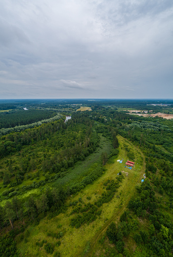Aerial view of a lush green forest landscape with a winding river and a small building in the foreground under a cloudy sky in Latvia. Aerial view of a lush green forest landscape with a winding river and a small building in the foreground under a cloudy sky in Latvia.