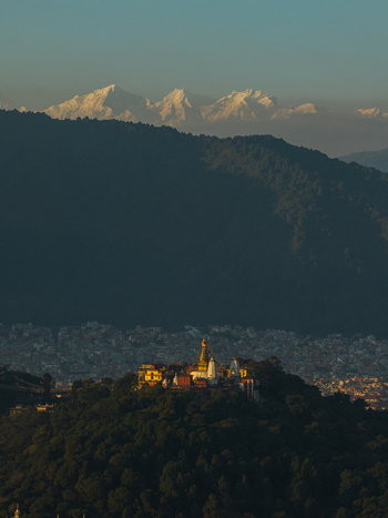 Aerial view of the Swayambhunath Stupa with its golden spire set atop a lush hill overlooking the Kathmandu valley with snow capped Himalayan peaks in the distance Nepal.